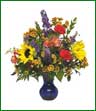 Bright colored sunflowers, carnations, alstroemeria and pompons arranged in a vase. Blue vase shown, but vase color may vary.