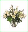 Long stemmed white roses and Casablanca lilies arranged in a glass vase.