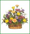 Roses, carnations, pompons and wax flower in shades of peach, yellow and lavender arranged in a basket.