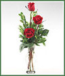 A simple vase of three red roses with ferns in glass vase.