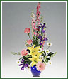 An elaborate vase of iris, larkspur, gerbera, roses, lilies and daisy spray mums. Vase color may vary.