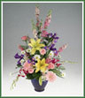 An elegant vase of mixed spring flowers with roses,  lilies, iris, larkspur, gerbera and daisy spray mums. Vase color may vary.