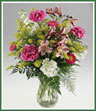 Stem length carnations, alstroemeria, stock, asters and solidaster fill a clear glass vase.