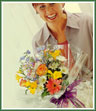 A cellophane-wrapped bouquet of flowers such as daisies, roses and freesia (when available) plus more.