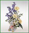 A novelty container with delphinium, carnations and daisy spray mums. Bear shown, but shape of container may vary.
