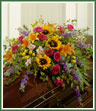 An abundant casket spray of sunflowers, lilies, roses, larkspur and stock.