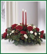 Share the joy this season with a festive fresh arrangement of red carnations and white pompons, winter greens and pinecones. Two red taper candles add seasonal charm to this centerpiece.