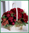 A handled basket carries red roses and red mini carnations accented with red glass ornaments and Christmas greens. Pepperberry and holly help to spread holiday cheer. Style of basket may vary.