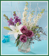 A traditional appeal with contemporary flair. White lilies and larkspur are paired with lavender roses and stock in a rectangular glass vase. White branches and limonium lend a festive air to an adventurous holiday bouquet. Style of vase may vary.