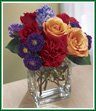Deep, vivid colors are the hallmark of this bouquet. Orange roses, red roses, and red carnations celebrate with shades of purple - purple aster, purple hyacinth, and purple statice. An ideal petite floral arrangement for any occasion. Style of vase may vary.