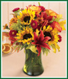 All the glorious colors of Fall are featured in this fabulous bouquet. Golden sunflowers and red Asiatic lilies are surrounded by Confetti roses, bronze daisy pompons and Matsumoto asters. A sprinkling of oak leaves and a basil hued vase complete the Autumn experience.