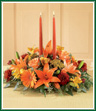 Bring all the colors of Autumn to your table for any Fall feast. Orange Asiatic lilies, Gerbera daisies and roses are beautifully complemented by gold alstroemeria, burgundy pompons and seeded eucalyptus. Two taper candles are included for a warm ambience. Color of candles may vary. 